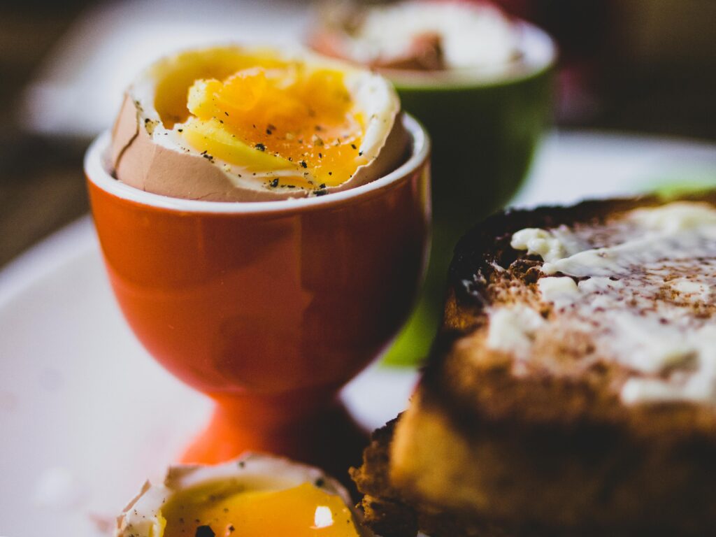 Close-up of a soft-boiled egg in a cup with buttered toast, perfect for breakfast.