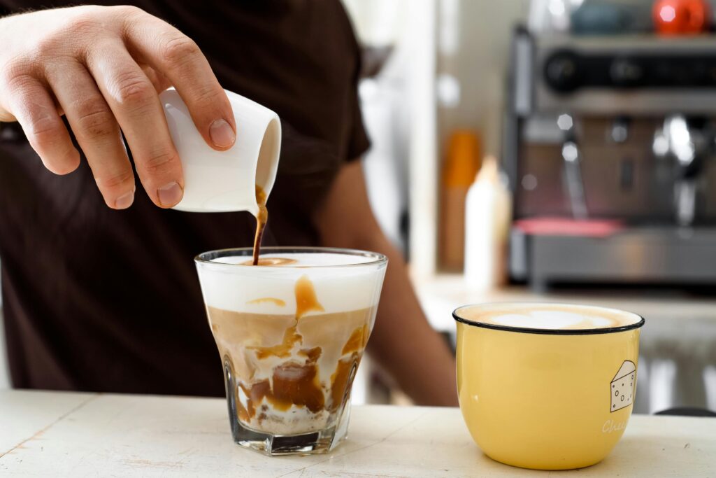 Hand pouring coffee into a frothy glass at a café in France, close-up view.